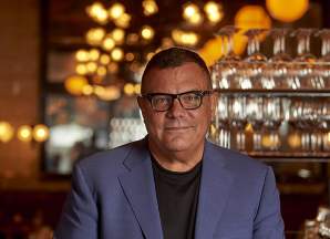 Stephen Starr stands with hands folded at a restaurant bar with decorative lighting overhead.