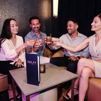 Young looking couples leisurely toasting with crafted cocktails seated at a low top table on plush seating at Nola's Lounge at Ocean Casino Resort in Atlantic City.
