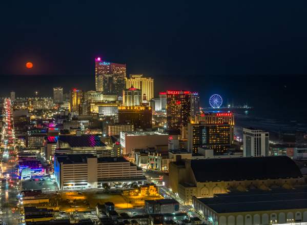Atlantic City skyline view at night with full moon rising above Absecon Inlet.