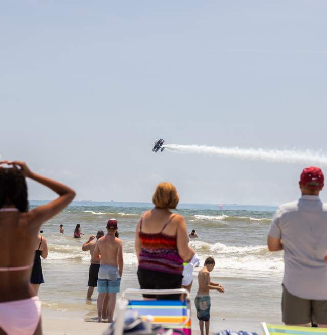 People standing on beach watching as planes perform maneuvers over the open ocean at the Soar & Shore Airshow in Atlantic City, NJ.