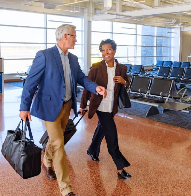 A man and woman walk through Atlantic City International airport terminal with rows of empty seats in the background.