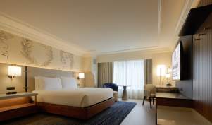 Hotel room at Caesars Atlantic City's Centurion Tower accommodations including a king size bed with warm woods and contemporary furnishings and window with view.