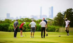 A golfer putts on a green on the Bay Course at Seaview with Atlantic City in distance.