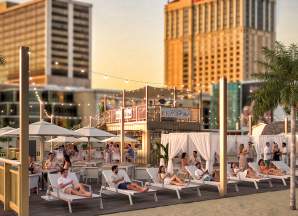 Rendering of Caesars Beach Club with people on lounge chairs elevated decks, palm tress and lighting just off the Boardwalk on the Atlantic City beach in front of Caesars Atlantic City.