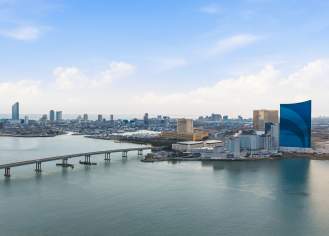 A long bridge stretches across a wide body of water toward the Atlantic City skyline featuring several tall hotels and skyscrapers under a bright blue sky.
