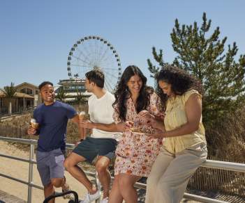 Group of young people hanging out eating ice cream on the Atlantic City Boardwalk with Steel Pier's ferris wheel and beach in background.