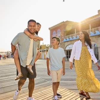 A father gives his child a piggy-back ride as others smile and laugh walking on the Atlantic City boardwalk as the sun sets behind Resorts Hotel and Casino.