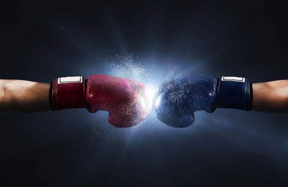 Two arms outstretched with one red and one blue boxing glove colliding in the center.