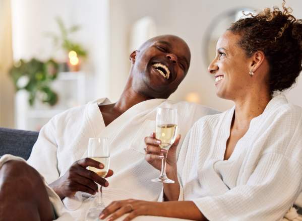 Two people laughing drinking Champagne in robes at a spa.