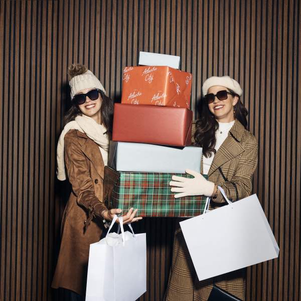 Two women hold up gift boxes and shopping bags at Tanger Outlets Atlantic City during the holidays.