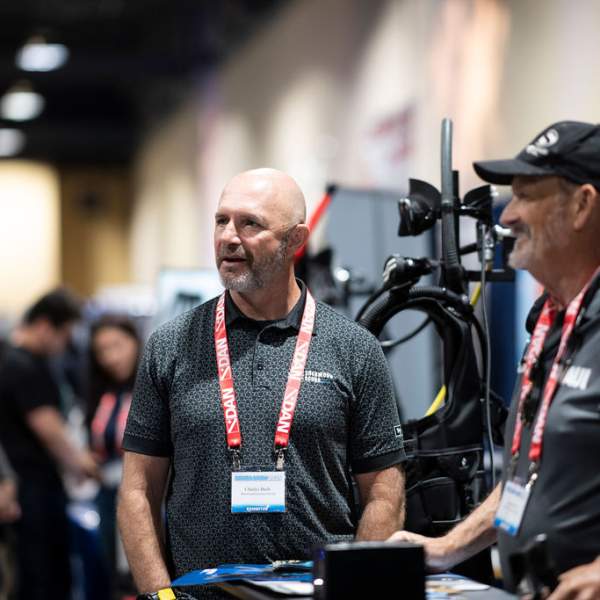Two exhibitors with lanyards talk with a show attendee at the Scuba Show.