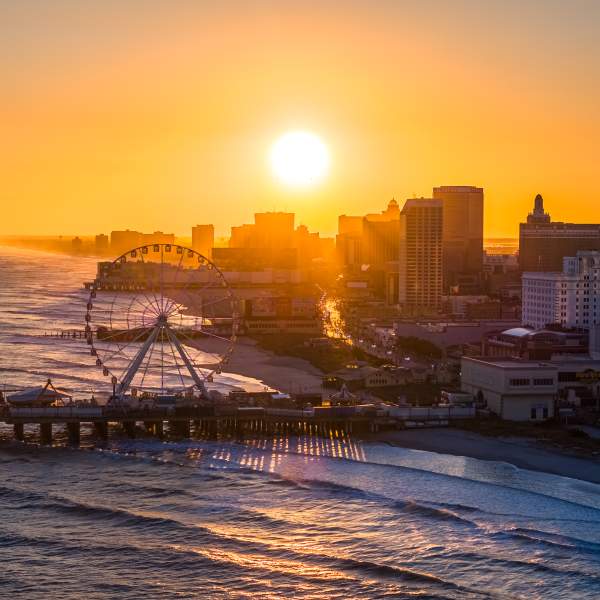 The setting sun shines over the Atlantic City skyline with the Steel Pier and ocean waves in the foreground.