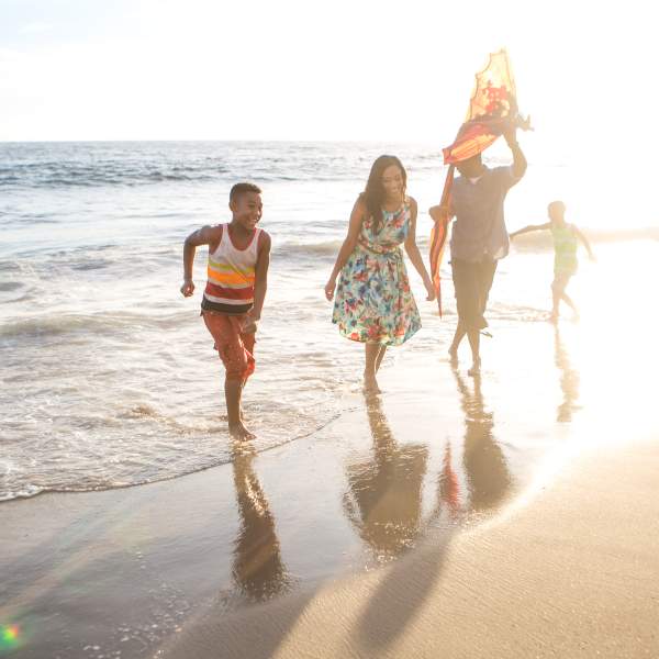 Family enjoying themselves in the shoreline of the beach with sun shining behind them.