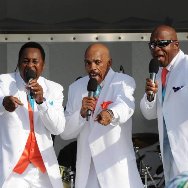 R & B singers in white suits on stage performing at a  Gardner's Basin Summer Concert Series concert.
