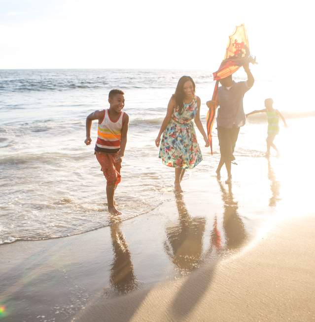 Family enjoying themselves in the shoreline of the beach with sun shining behind them.