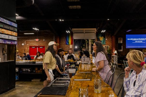 Woman orders a craft beer at the bar inside Savannah River Brewing Company while guests gather and socialize in the brewery's taproom in Augusta, Georgia.