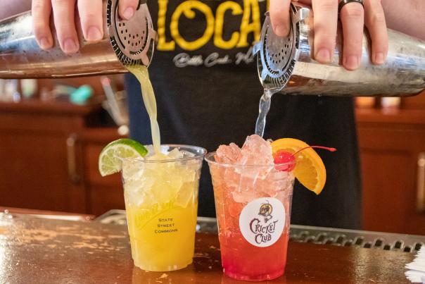 Bartender pouring a cocktail over ice next to yellow and red citrus-garnished drinks at Cricket Club in Calhoun County.