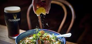 Lemon being squeezed over Seafood Chowder with a pint of Guinness int he background