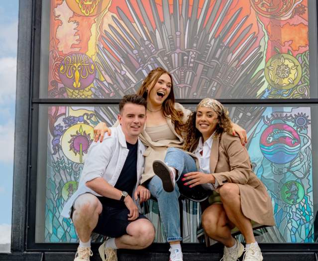 Group of three people posing for a phone at one of the stained glass windows on the Glass of Thrones Trail.
