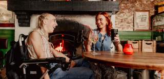 Two women having drinks in a pub beside the fire.