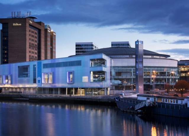 Photo of the waterfront hall in Belfast overlooking the water with the Hilton hotel in the background.