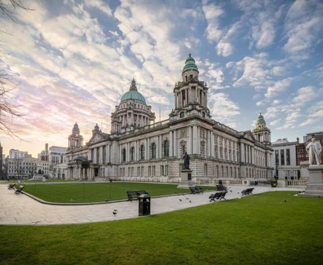Photo of Belfast City Hall from outside looking at the grass areas and benches.