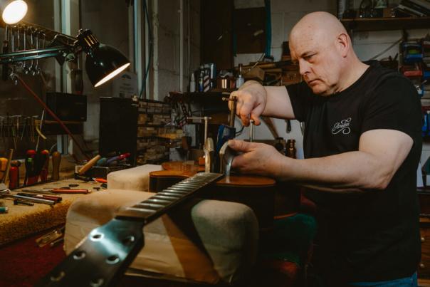 Man in a workshop fixing a guitar.