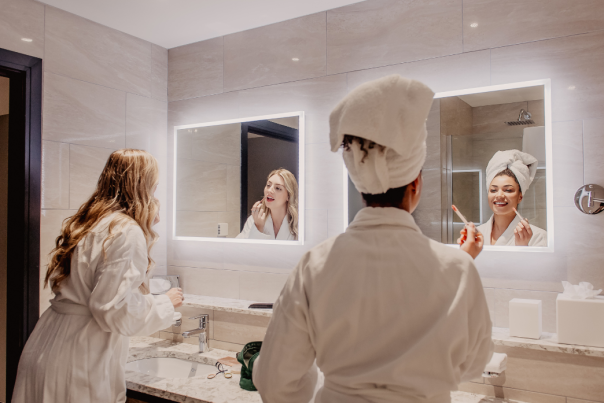Image of two girls getting ready in robes at a spa. They are doing their makeup in the mirror together.