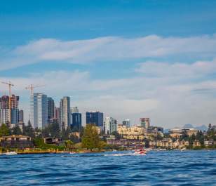Bellevue skyline view with modern skyscrapers and construction, set against a blue sky and a calm Lake Washington in the foreground.
