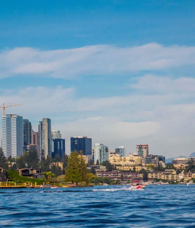 Bellevue skyline view with modern skyscrapers and construction, set against a blue sky and a calm Lake Washington in the foreground.
