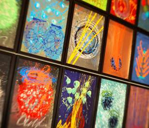 A vibrant collage of abstract paintings in black frames, showcasing dynamic swirls, shapes, and splashes of paint on dark backgrounds.