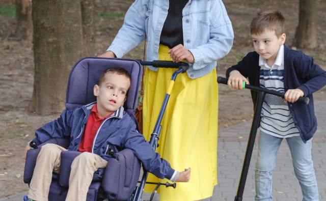 Mom walking with her kids, one on a scooter and the other in a wheelchair