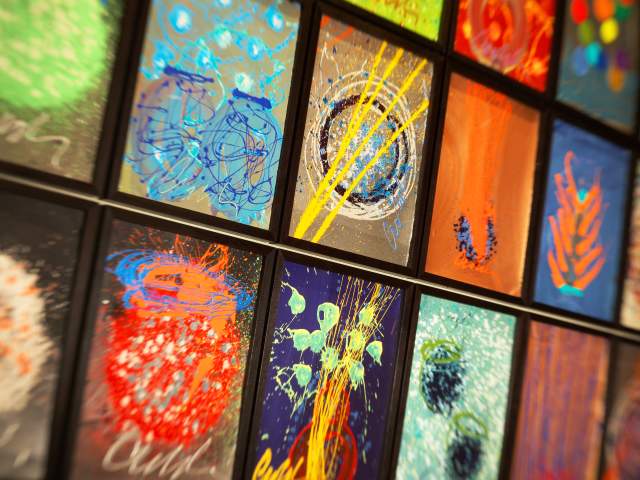 A vibrant collage of abstract paintings in black frames, showcasing dynamic swirls, shapes, and splashes of paint on dark backgrounds.