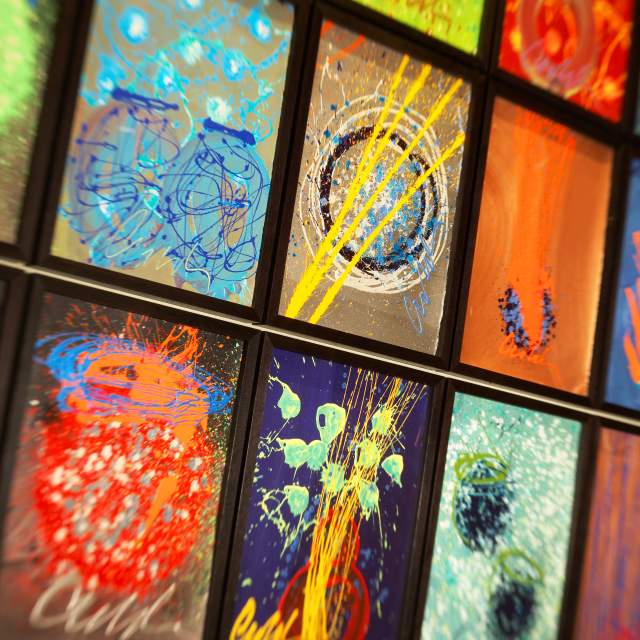 A vibrant collage of abstract paintings in black frames, showcasing dynamic swirls, shapes, and splashes of paint on dark backgrounds.