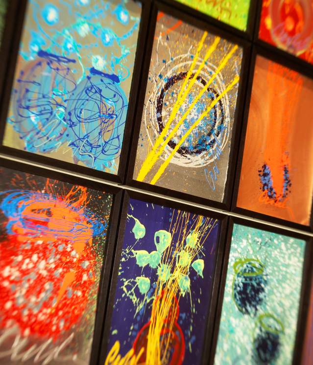 A vibrant collage of abstract paintings in black frames, showcasing dynamic swirls, shapes, and splashes of paint on dark backgrounds.