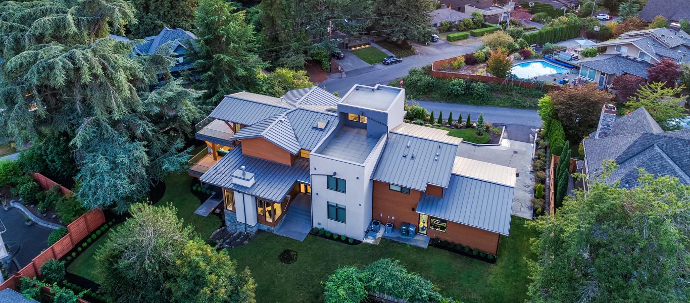 Modern and rustic home, with wood siding, metal roof, nestled between evergreens and view of the lake