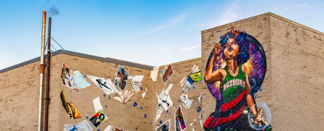 Mural depicting child wearing a dress reading Roxbury blowing bubbles and surrounded by blowing posters and books