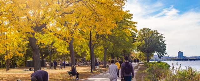People sitting on benches and others walking on paved path along the Charles River Esplanade of Boston