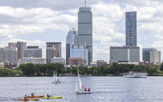 A few kayaks and sailboats on the Charles River with the Boston skyline in the background