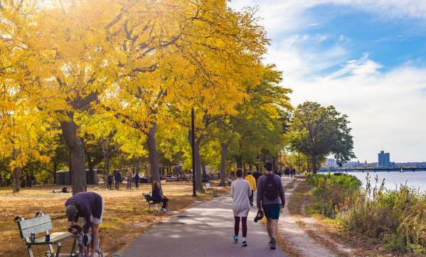 People sitting on benches and others walking on paved path along the Charles River Esplanade of Boston