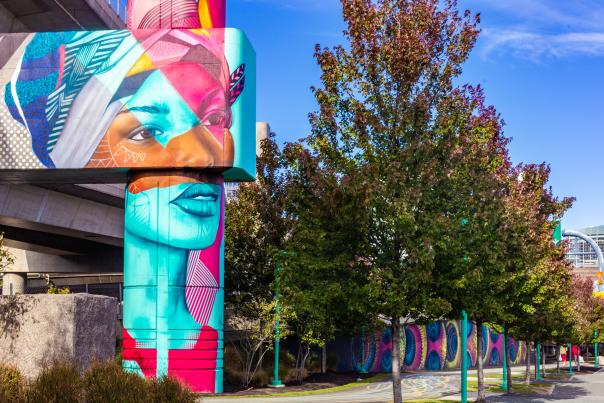 Woman's face with geometric shapes in turquoise, terracotta and magenta, painted on a cement column.