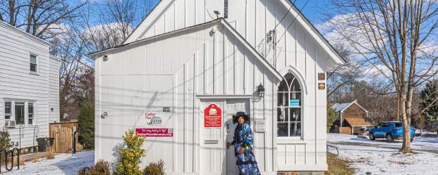 Exterior view of a small white church building in Bucks County with a person standing at the entrance on a snowy day.