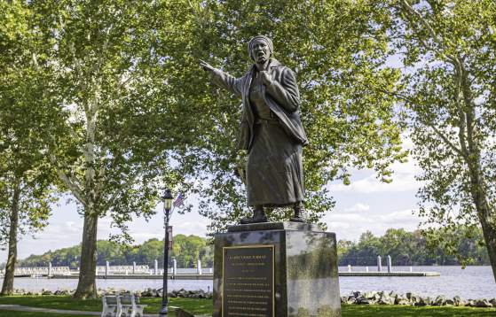 Statue in a Bucks County park depicting a historical figure pointing forward, set among trees with a river in the background.