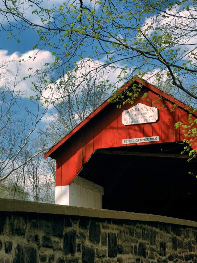 The bright red paint of Frankenfield Covered Bridge shines bright among the greens on a spring day. The bridge is one of 12 remaining covered bridges in Bucks County.