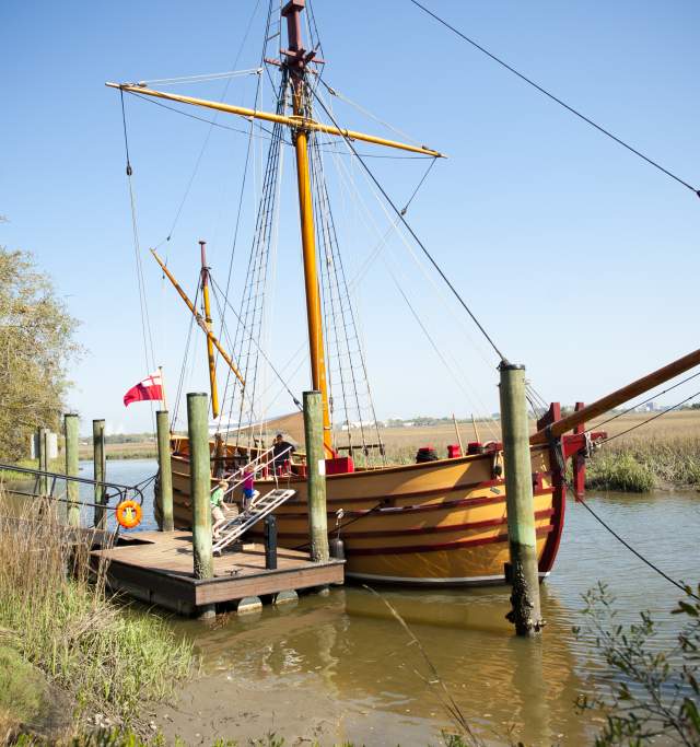 A wooden boat rests at the dock, surrounded by gentle waves and a clear sky.