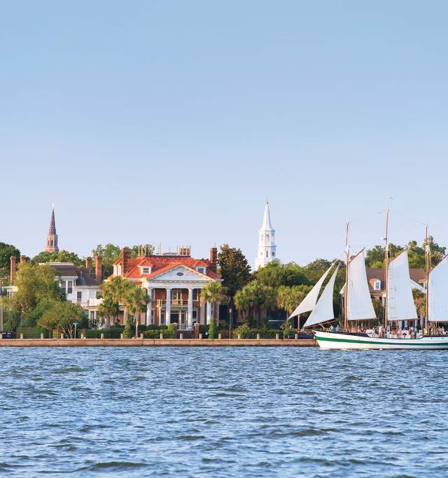 A sailboat in a body of water with houses and trees in the background