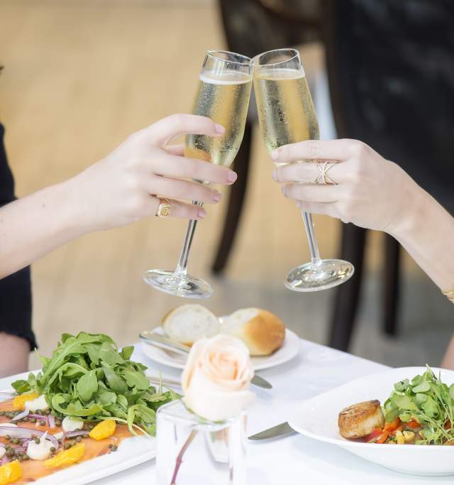 Two ladies toast with champagne glasses, having dinner and surrounded by a celebratory atmosphere