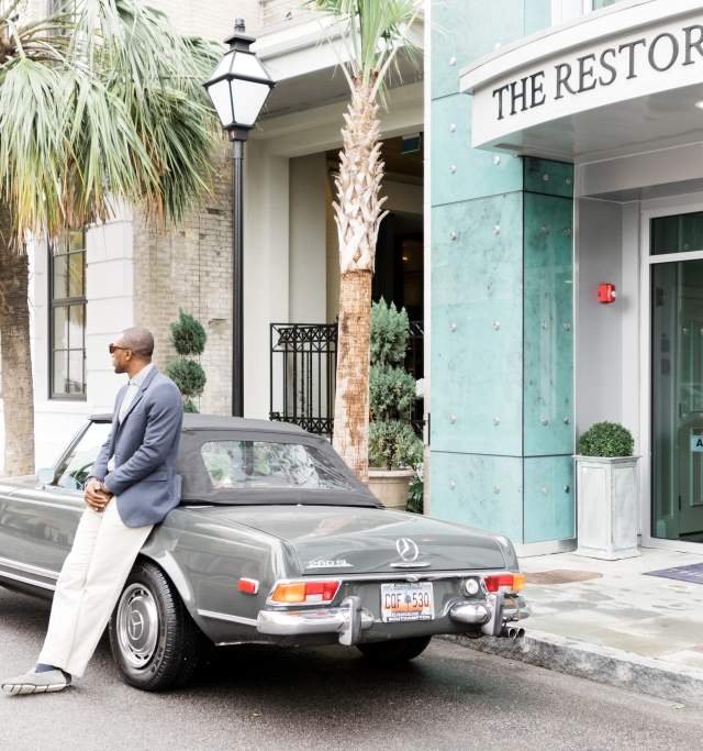 A man perched on the hood of a car, appearing relaxed as he gazes into the distance.