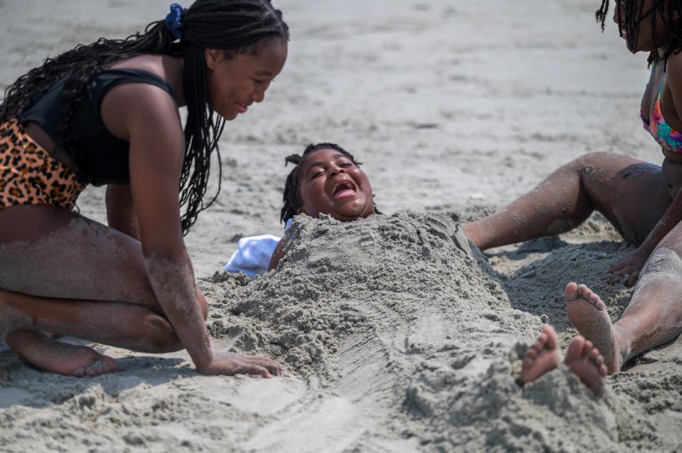 Three kids laughing while playing in the sand at the beach.