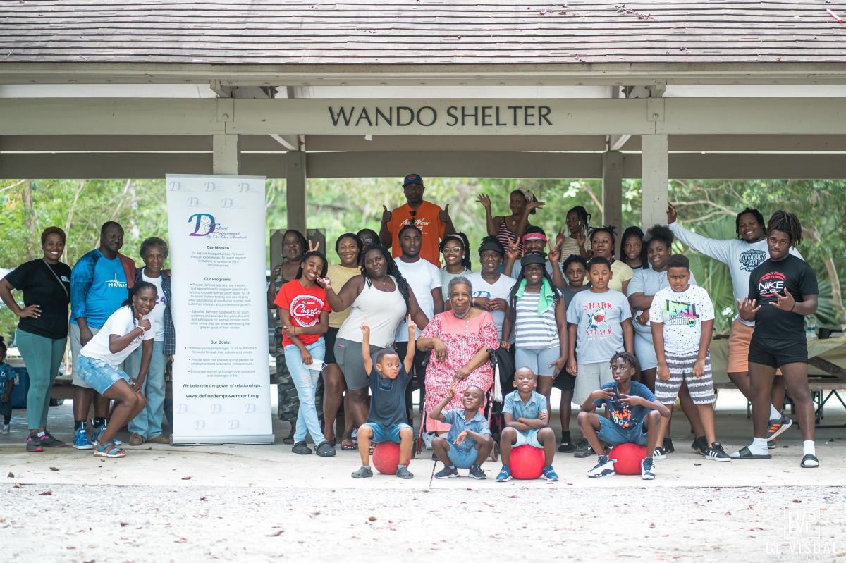A group of people pose for a picture with a banner while under a covered shelter.